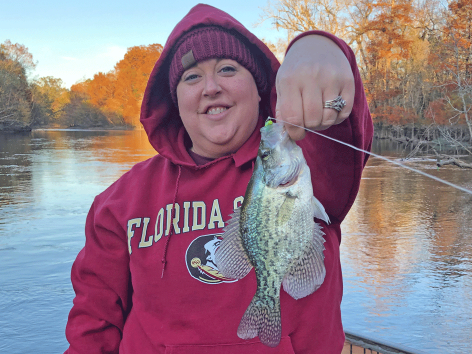 A smiling angler holding Crappie (Speckled Perch) with trees and water behind her, Florida.