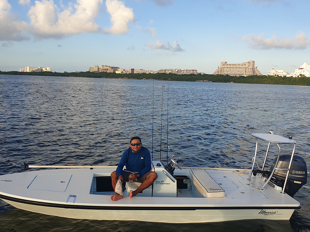 Риболовец, седнал на плоска лодка с Канкун на заден план.