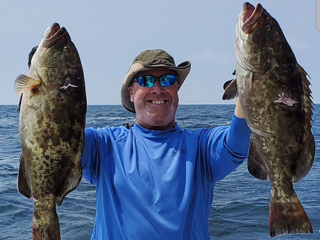 A smiling angler holds up a pair of Groupers he caught during a fishing trip near Morehead City.