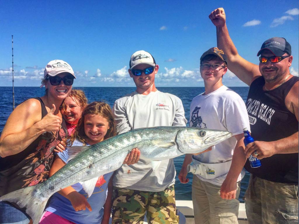 A group of anglers gathered around their captain who is holding Barracuda