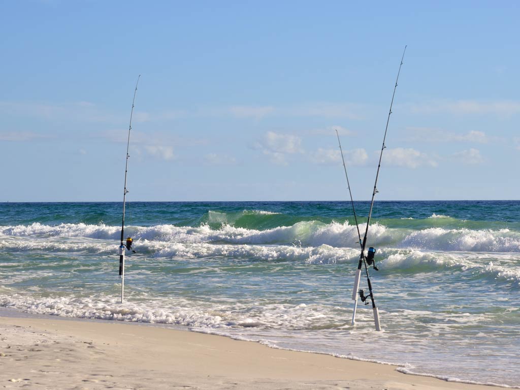 A photo of the beach, with waves crashing into the sand where a couple of fishing rods are stationed