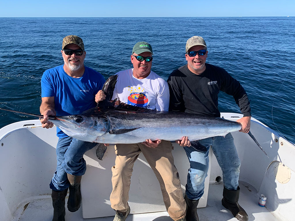 Three anglers hold a large Marlin caught while fishing in North Carolina during deep sea fishing season