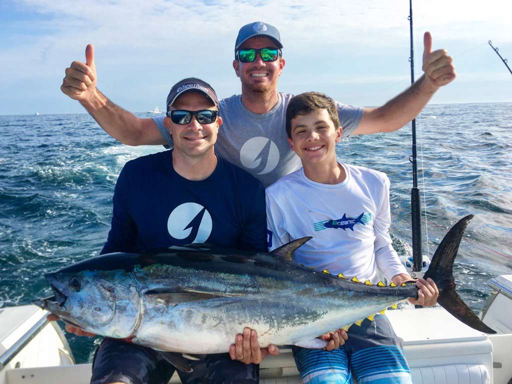 Three men posing on a boat with a huge Bluefin Tuna.