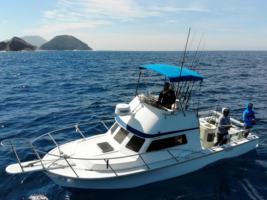 An aerial view of a fishing charter in Southern California with the captain on the flybridge and two anglers casting a line over the side of the boat