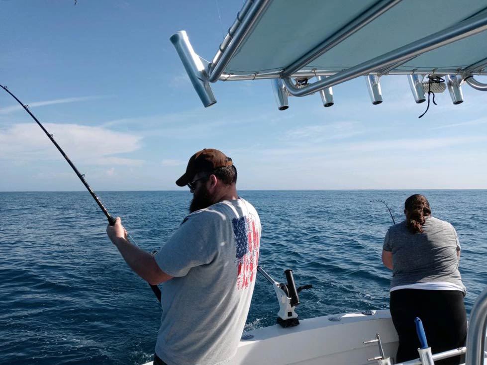 A picture showing two anglers, one male and one female, each busy reeling in fish with fishing rods while standing on a charter fishing boat in Cape Canaveral, Florida