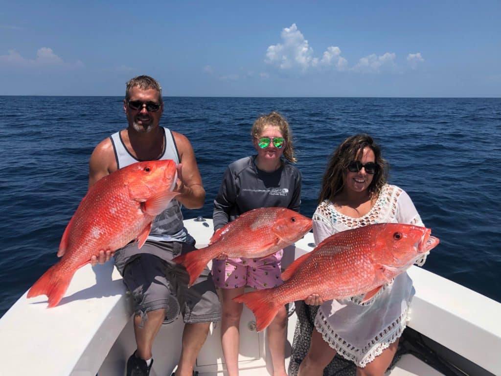 A picture showing three anglers, one male and two female, each holding Red Snapper while standing on a charter fishing boat in Cape Canaveral, Florida