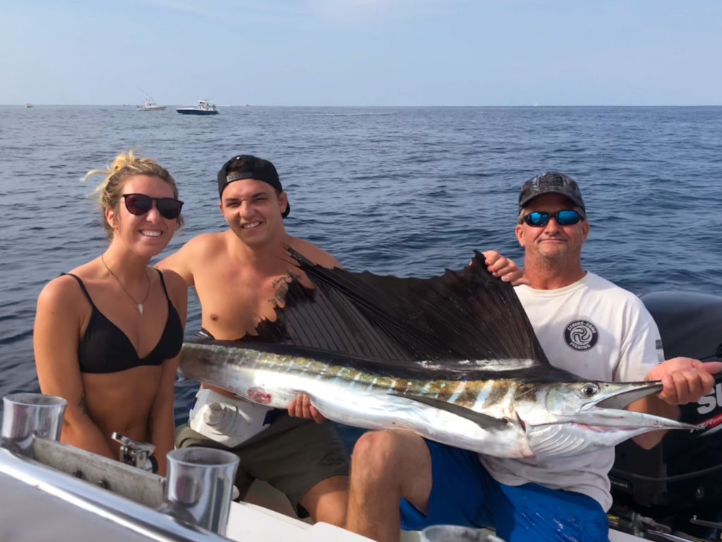 A picture showing the waters of Cape Canaveral, Florida, and three anglers, one female and two male, with two of them holding a freshly caught Billfish 