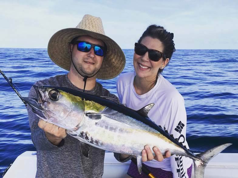 A picture showing a couple of smiling anglers on a fishing boat in Cape Canaveral, where one of them is holding a freshly caught Tuna