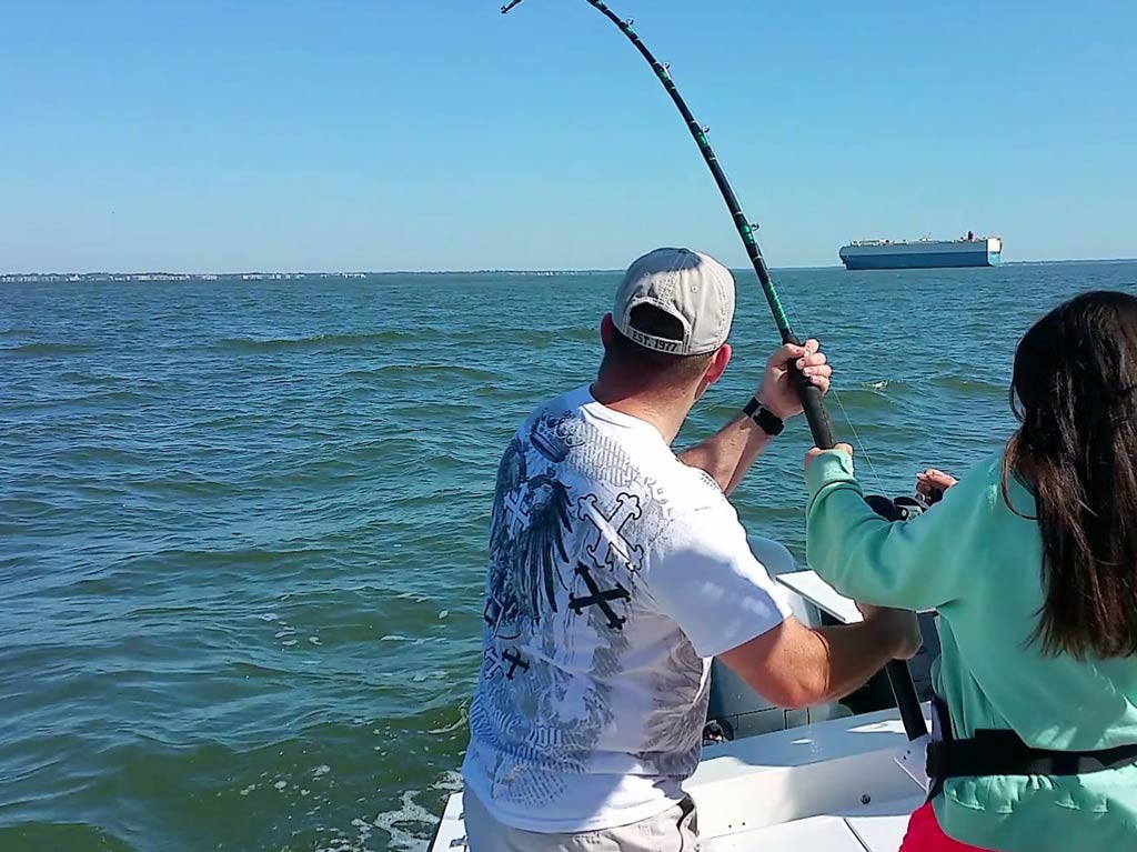 A view from behind of a captain helping an angler while standing on a charter fishing boat and bottom fishing