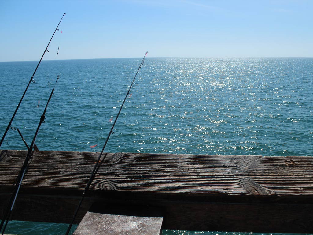 Three rods left on a fishing pier on a cloudless day