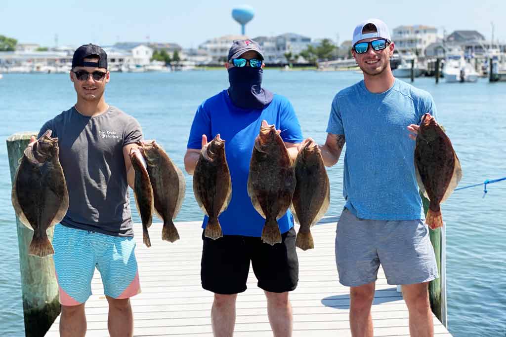 Three men standing on a dock, holding their daily catch of Flounder on a sunny day