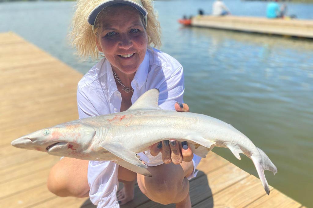 A smiling middle-aged woman standing on a dock, holding a small Blacktip Shark