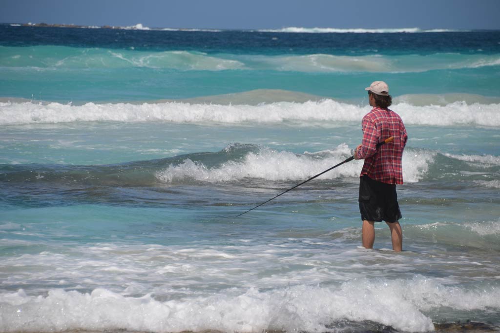 A surf angler standing in the waves with a fishing rod in his hand on a summer's day