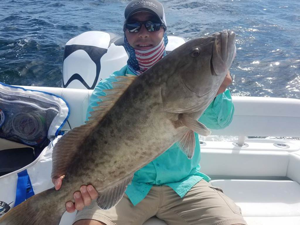 An angler sitting on a charter boat and holding a Gag Grouper with both his hands