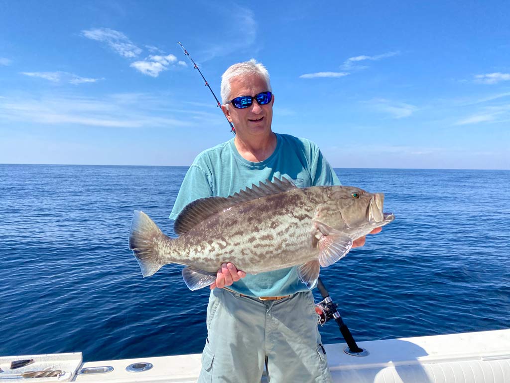 An elderly angler on a boat, holding a Gag Grouper caught deep sea fishing in Fernandina Beach.