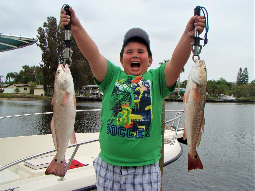 A photo of a happy kid standing and holding a fish in each hand caught while fishing in Bradenton