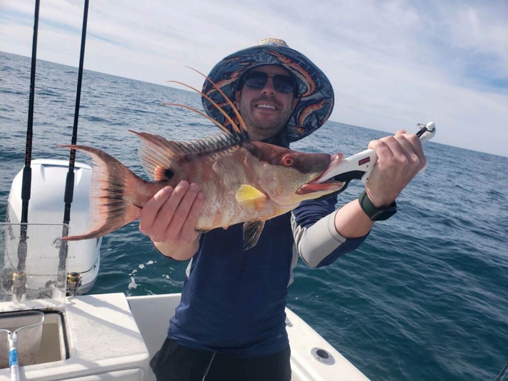 A photo of a satisfied angler holding a Hogfish with both his hands while standing on a charter fishing boat