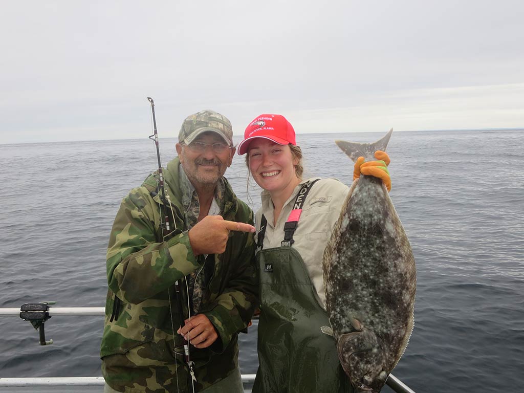 A female angler holding a Halibut while a man stands next to her on a fishing charter in Homer, AK