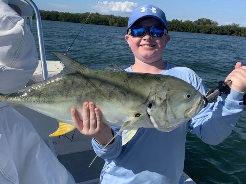 A kid standing on a charter boat and holding a Jack Crevalle