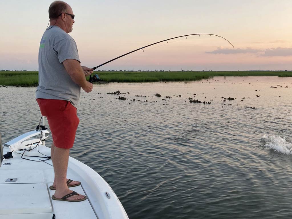 A side view of an angler holding a rod and fishing while standing on a charter fishing boat