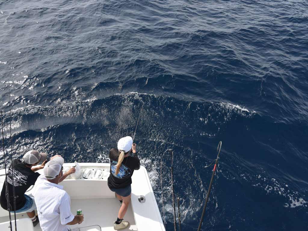 A photo of a woman fighting a fish on a charter boat, with two men behind her.