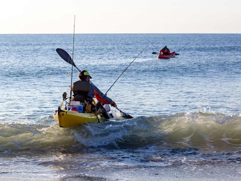 Two kayak anglers setting off on a fishing trip from a beach.