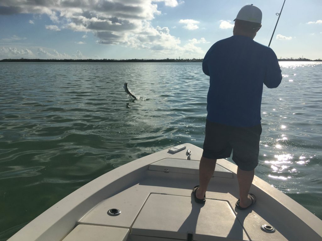 A picture showing a male angler trying to catch a leaping Tarpon, while standing on a fishing boat in Key West, Florida