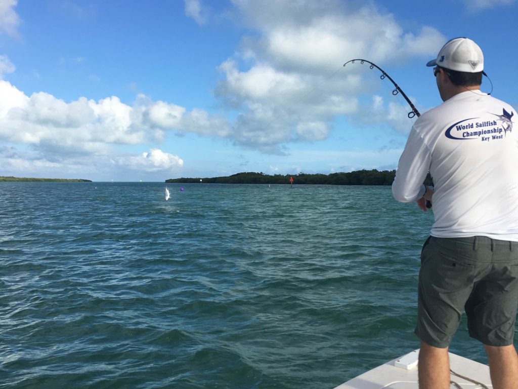 A male angler standing on a boat in Key West, Florida, fishing for a Tarpon that's leaping out of the water in front of him