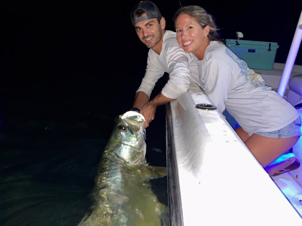 Two anglers, one male and one female, both smiling, while the male angler is holding a freshly-caught Tarpon in the water in Key West, Florida