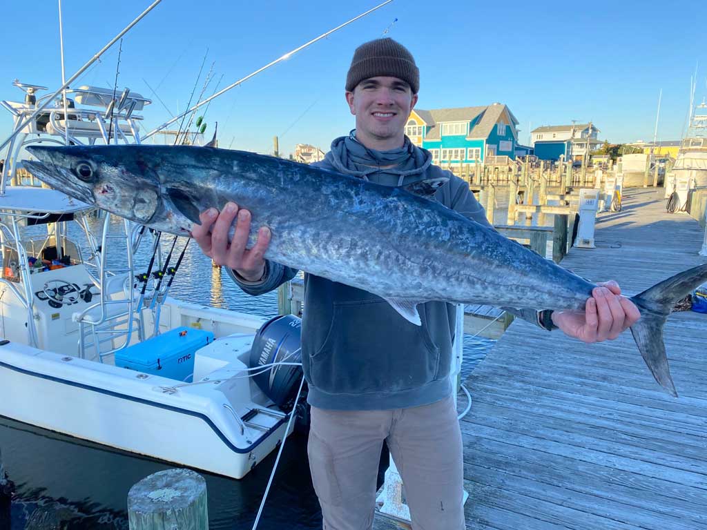 An angler standing on a dock, holding a big King Mackerel he caught while fishing offshore from Oregon Inlet.