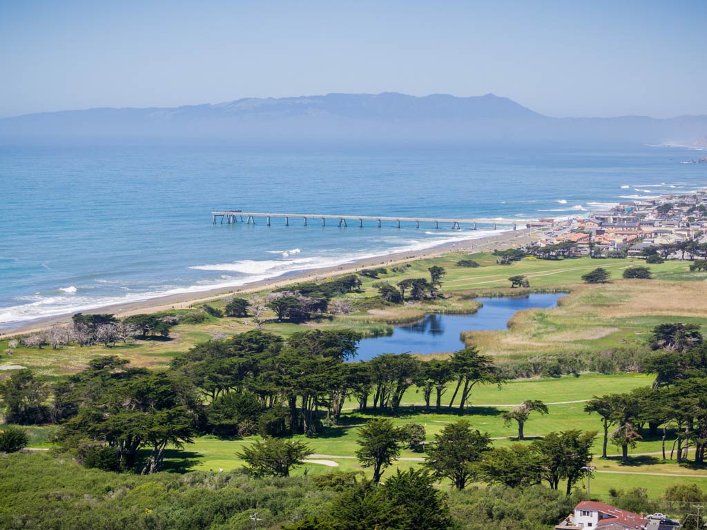 An aerial view of Pacifica’s Municipal Pier against the blue water and green inland area