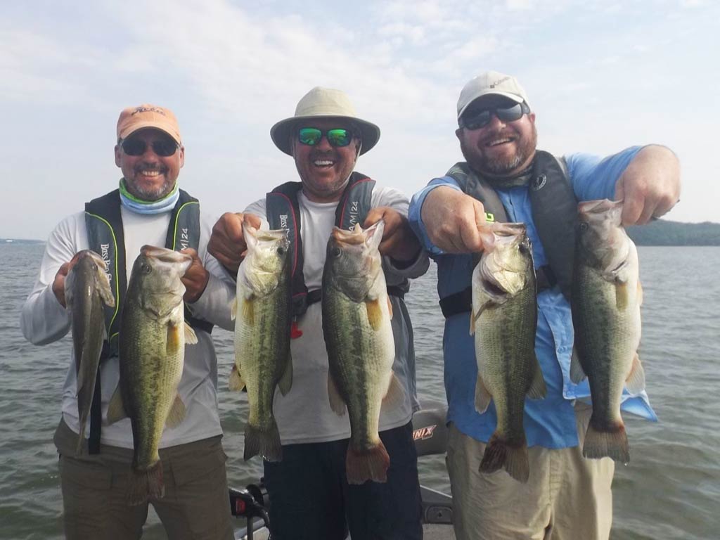 A trio of happy anglers holding a couple of Bass each with both hands and smiling while standing on a Paducah fishing charter