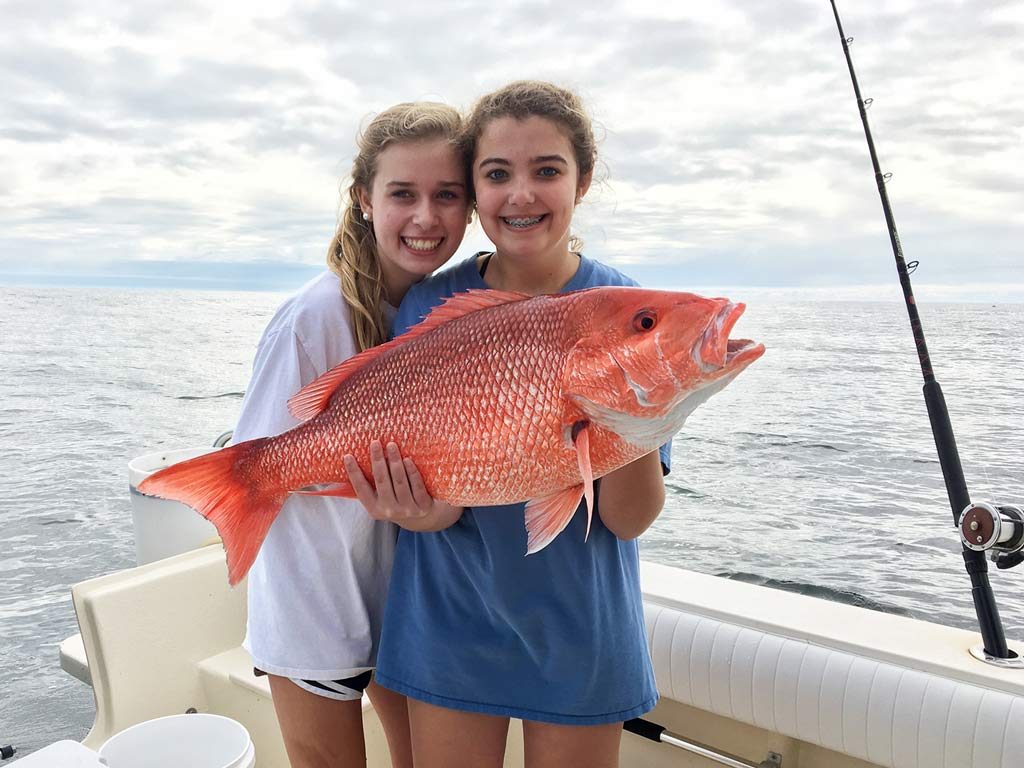 Two girls on a boat, holding a big Red Snapper they reeled in fishing offshore from Fernandina Beach.