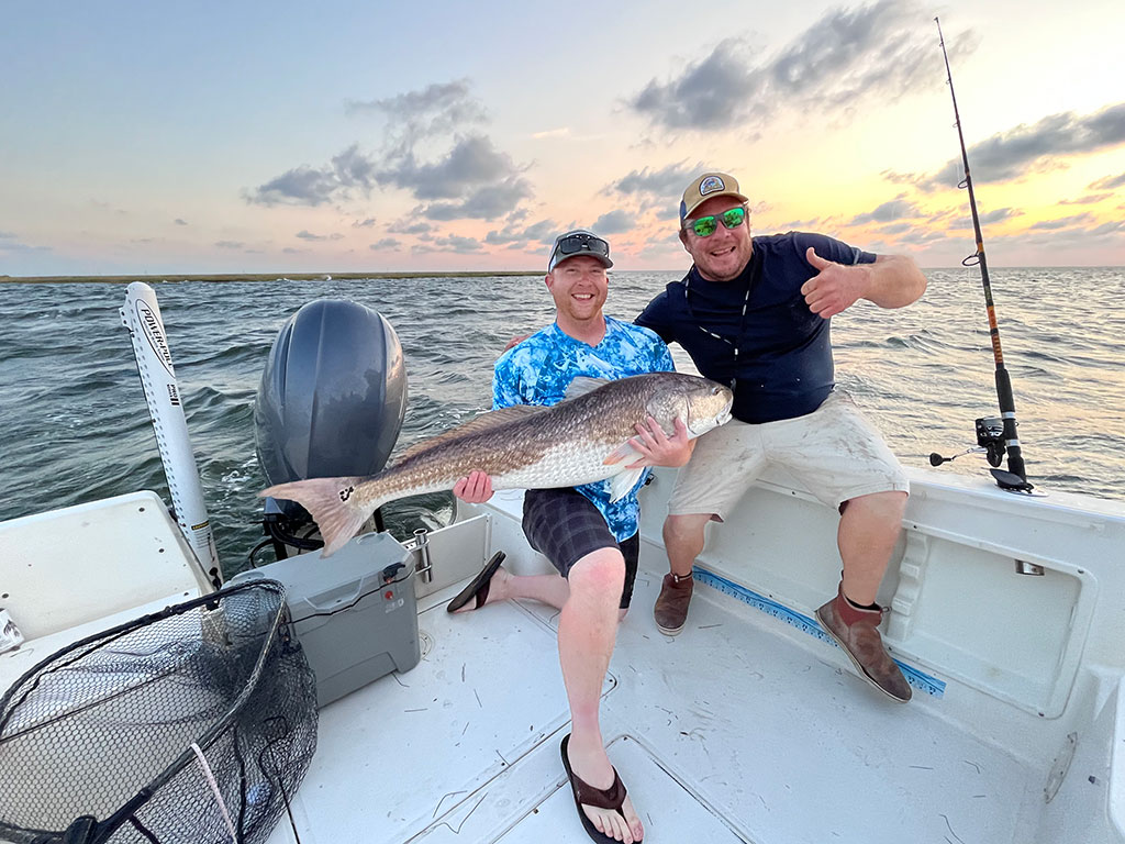 Two anglers on a boat hold a large Bull Redfish caught in North Carolina in the fall