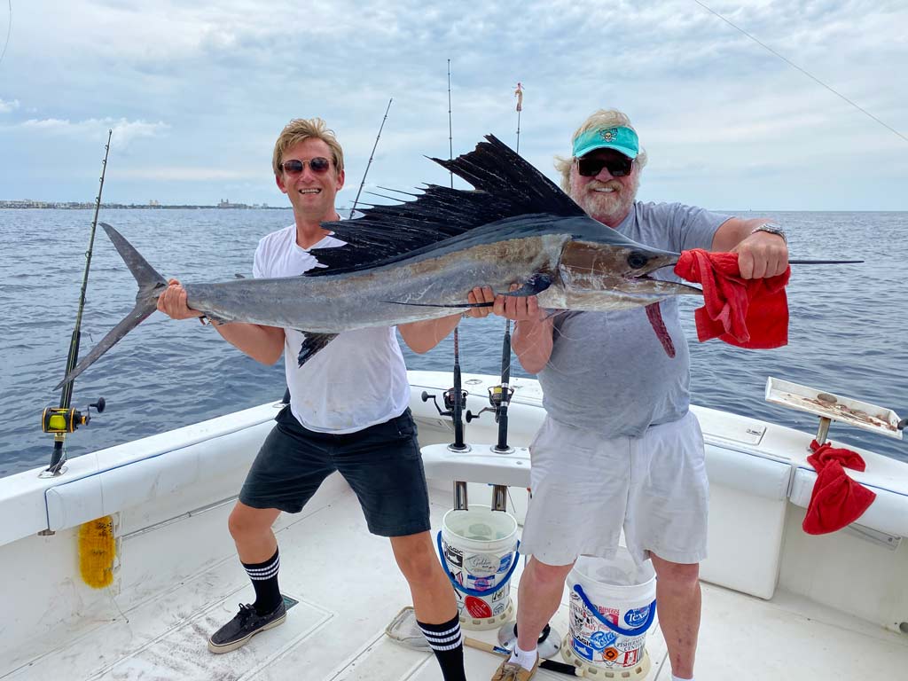 Two anglers standing on a boat deck, smiling and holding a huge Sailfish.