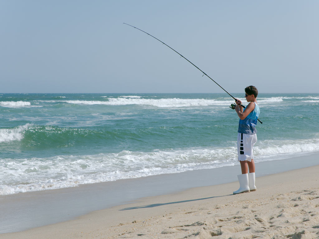 A young angler fishing from a beach in New Jersey on a sunny day.