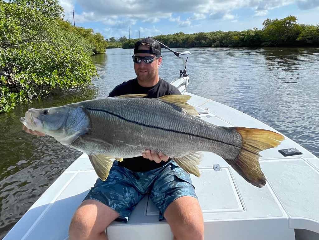 An angler sitting on a boat, holding a huge Snook he caught fishing in Jupiter.