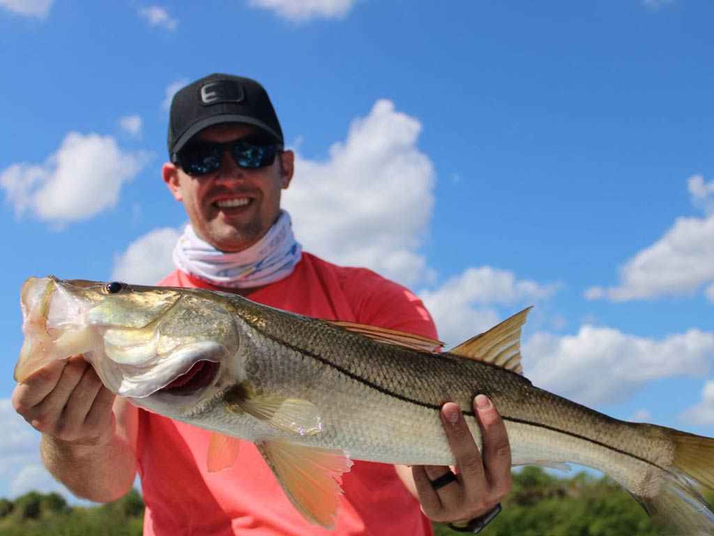 An angler holding a Snook with both hands caught while fishing in Bradenton on a bright and sunny day
