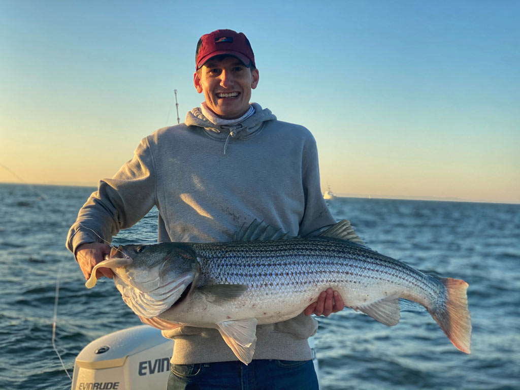 A smiling angler holding a big Striped Bass caught fishing in Ocean City, NJ.