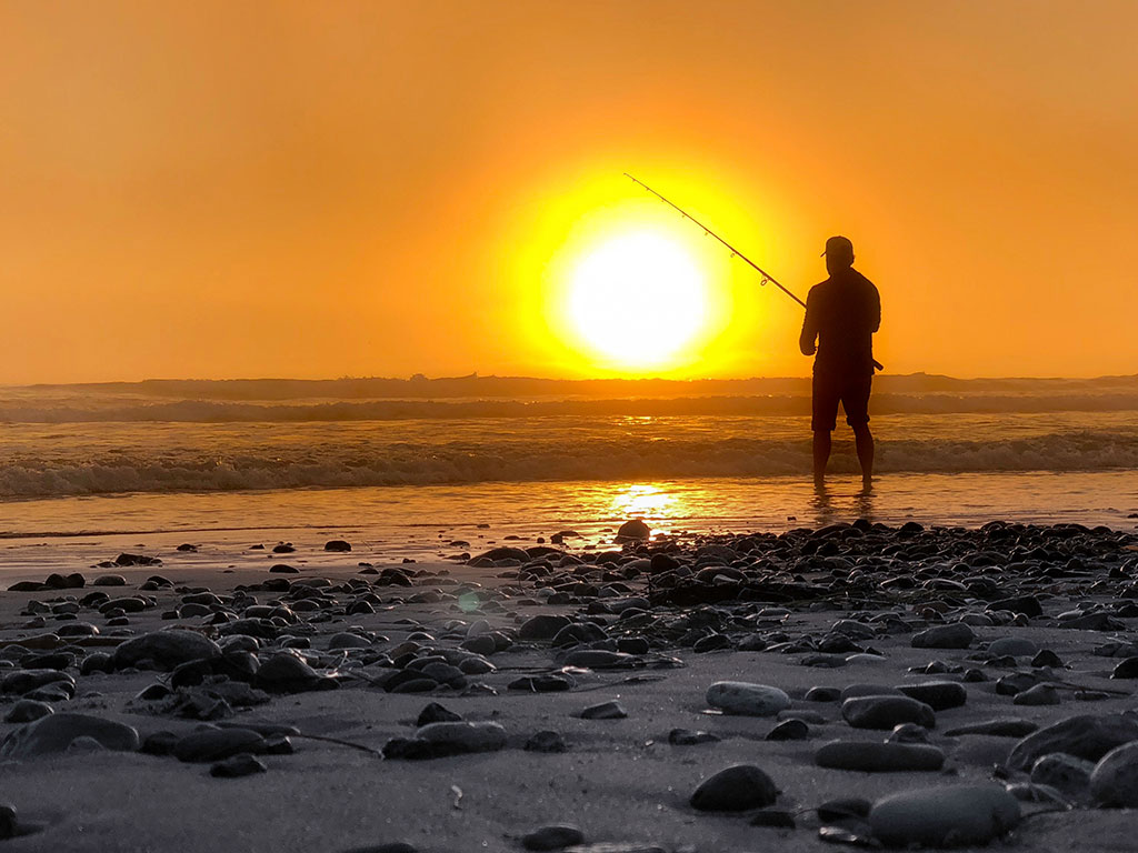 An angler casts a line into the surf at sunset in Southern California