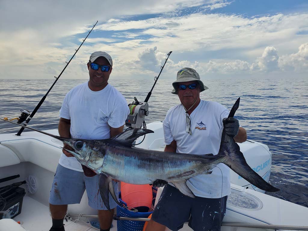 A pair of anglers on a charter boat, posing with a Swordfish they successfully caught.