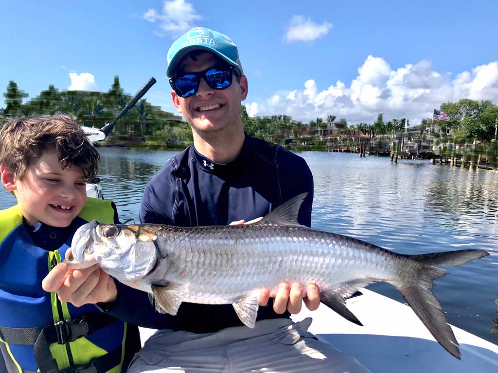 A man and a boy on a boat, posing with a juvenile Snook they caught on a Jupiter Inlet fishing trip.