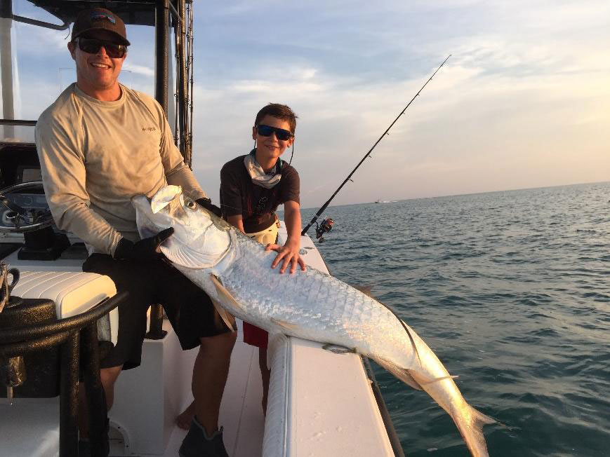 An elder and younger angler hold a large Tarpon at the side of a boat in North Carolina