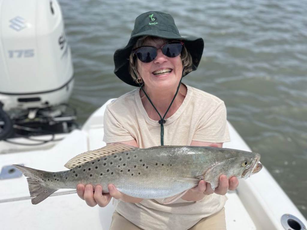 A photo of an angler sitting on a boat and holding a Spotted Seatrout caught while fishing in Jekyll Island’s waters