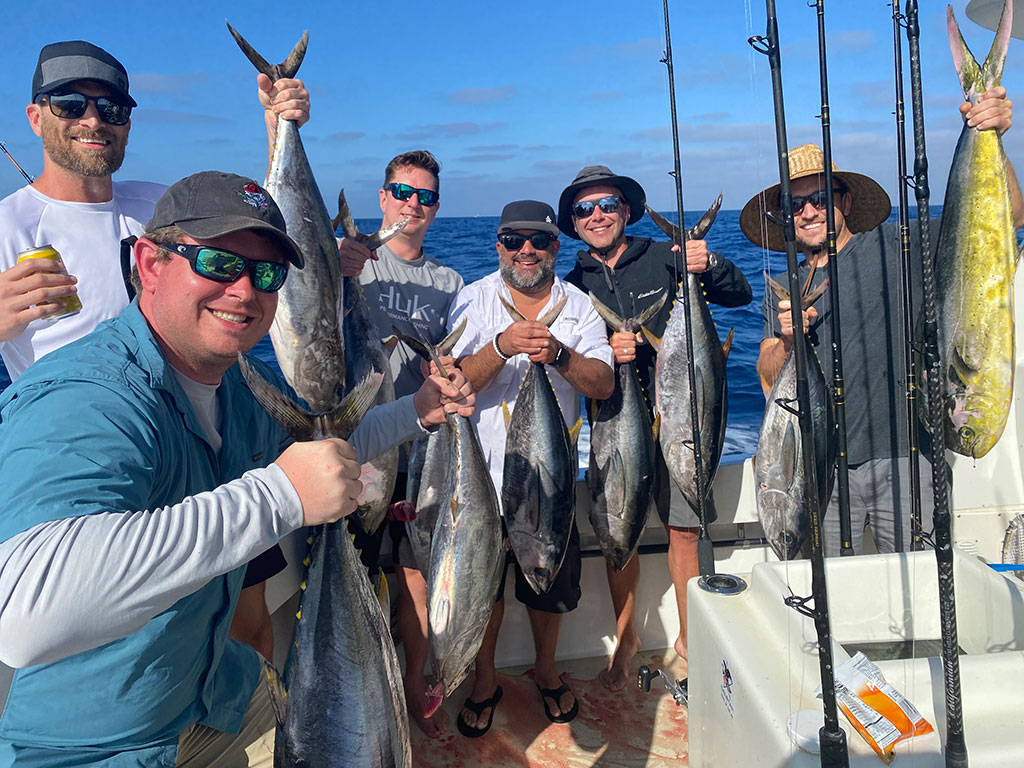 A group of anglers on a fishing charter hold a Tuna each on a sunny day