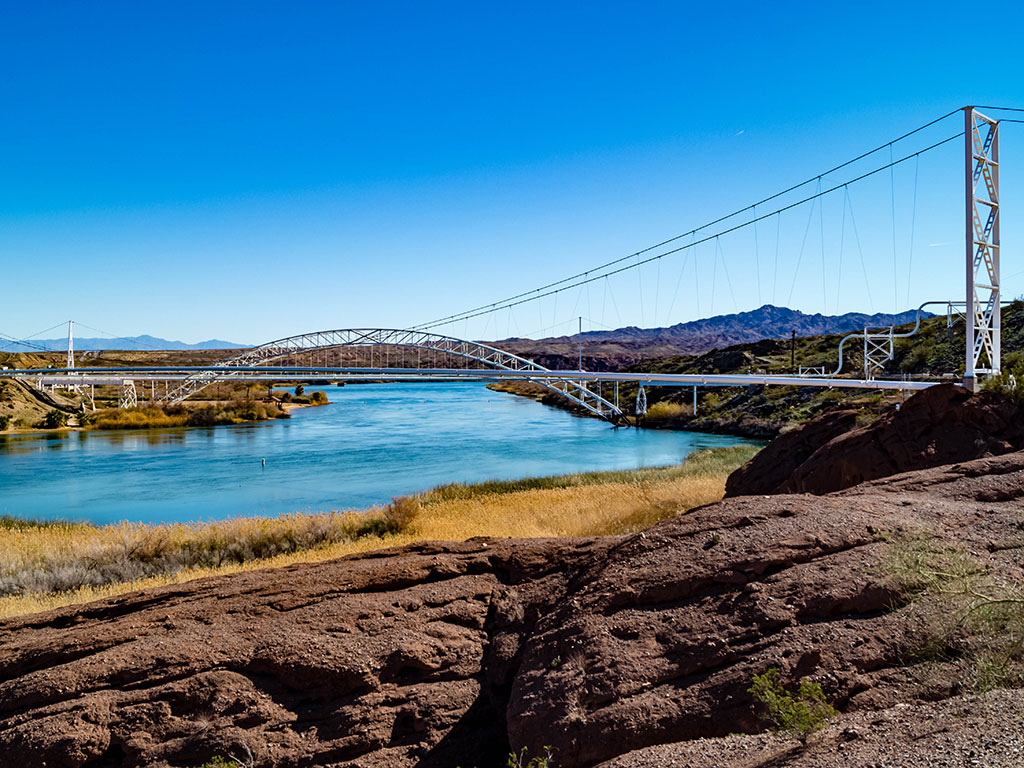 A view from a hill of a bridge connecting Arizona and California across the Colorado River on a sunny day