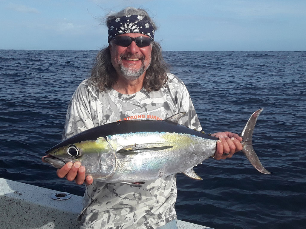 A smiling angler on a bandana holds a Tuna he recently caught on an offshore trip out of Morehead City.