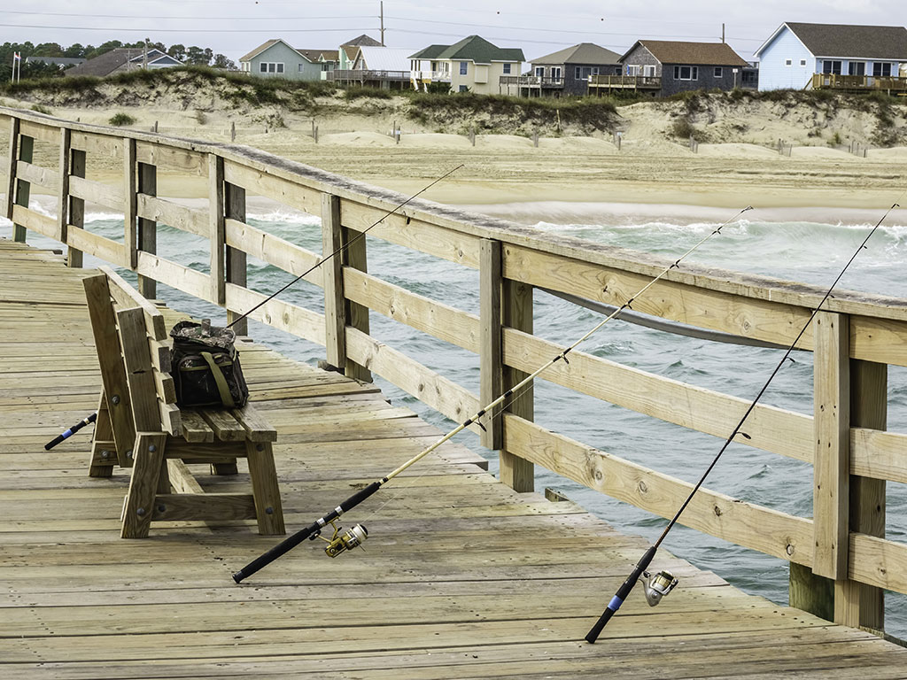 A bench on a fishing pier next to which are three fishing rods.