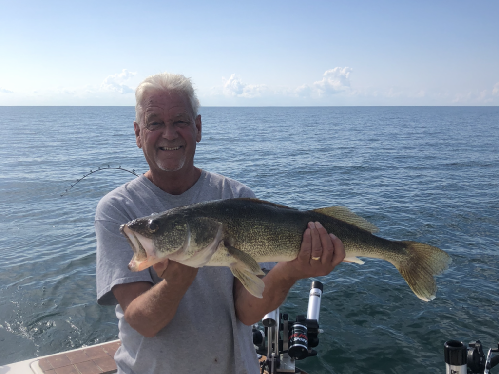 A happy male angler standing on a charter fishing boat and holding a freshly caught Walleye, Michigan