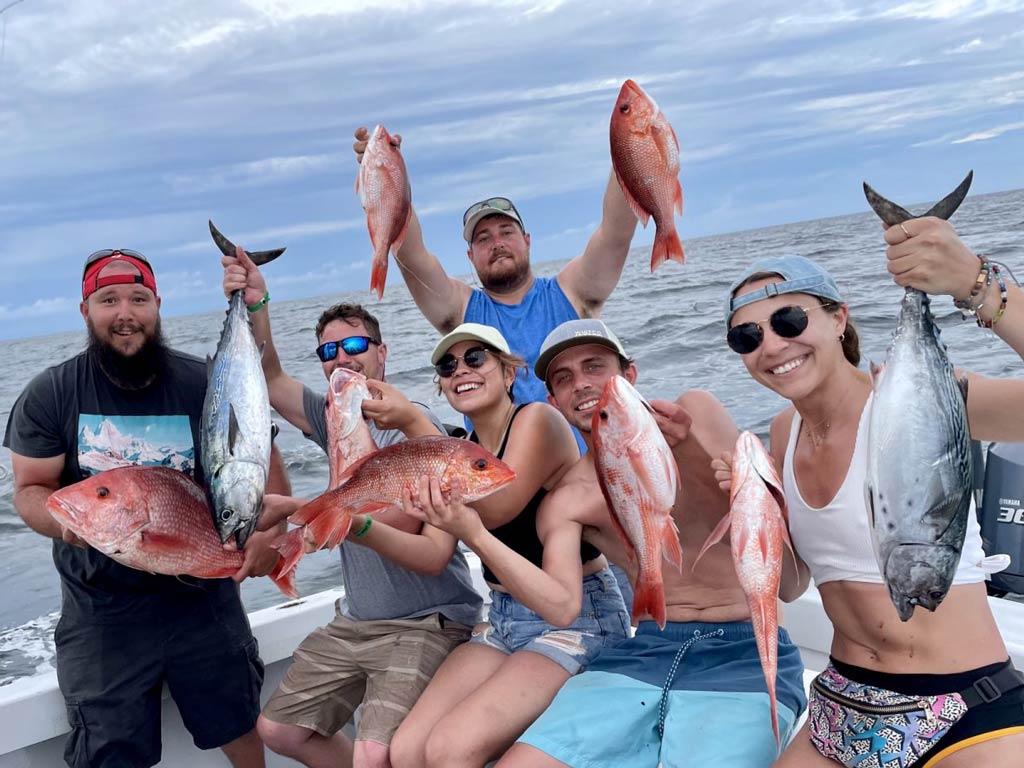 A group of satisfied anglers sitting on a fishing charter boat and holding their Snapper and Tuna catches on a cloudy day